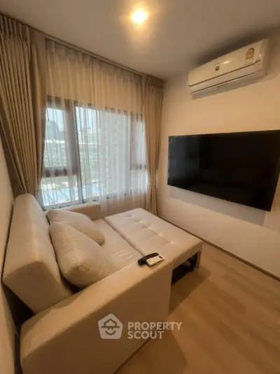 Cozy living room with modern sofa and wall-mounted TV, featuring large windows and air conditioning.