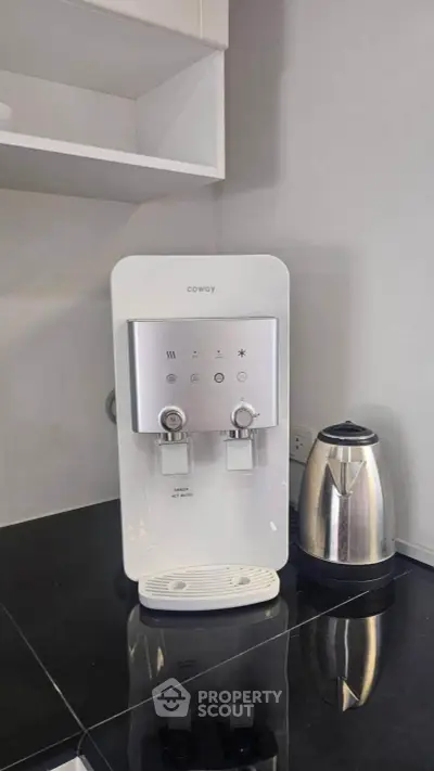 Modern kitchen corner with sleek water dispenser and electric kettle on black countertop.