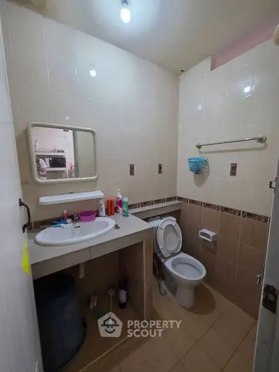 Compact bathroom with tiled walls, sink, and toilet, featuring essential toiletries and a mirror.