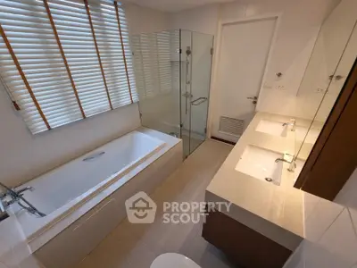Modern bathroom with bathtub, glass shower, and dual sinks in a stylish home.