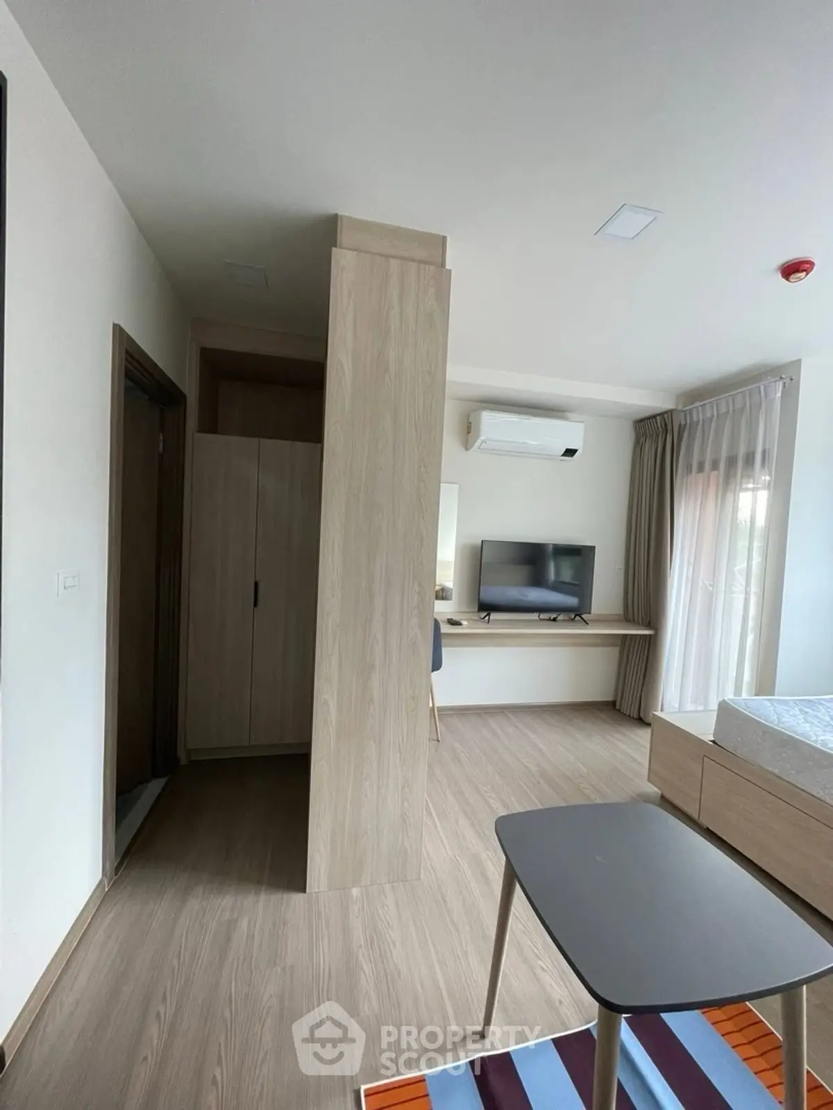 Modern studio apartment with sleek wooden flooring and wall-mounted TV, featuring a cozy layout.