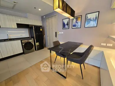 Modern kitchen with sleek black dining table and stylish chairs, featuring built-in appliances and elegant lighting.