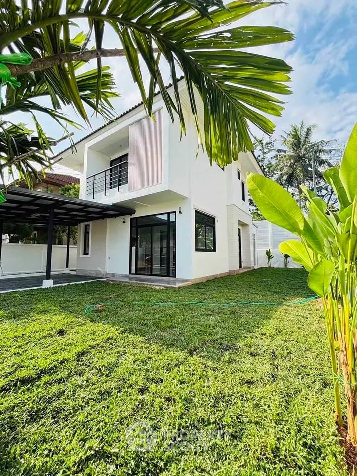 Modern two-story house with lush green lawn and tropical plants