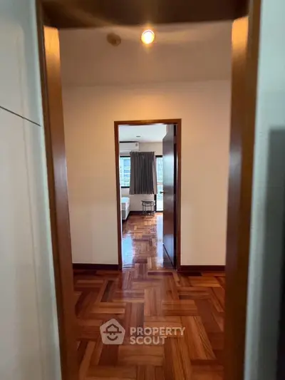 Spacious apartment hallway leading to a cozy bedroom with wooden flooring and natural light.