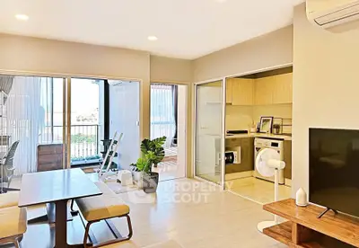 Modern living room with open kitchen and balcony view, featuring stylish furniture and natural light.