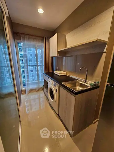 Modern compact kitchen with washing machine and city view from window.