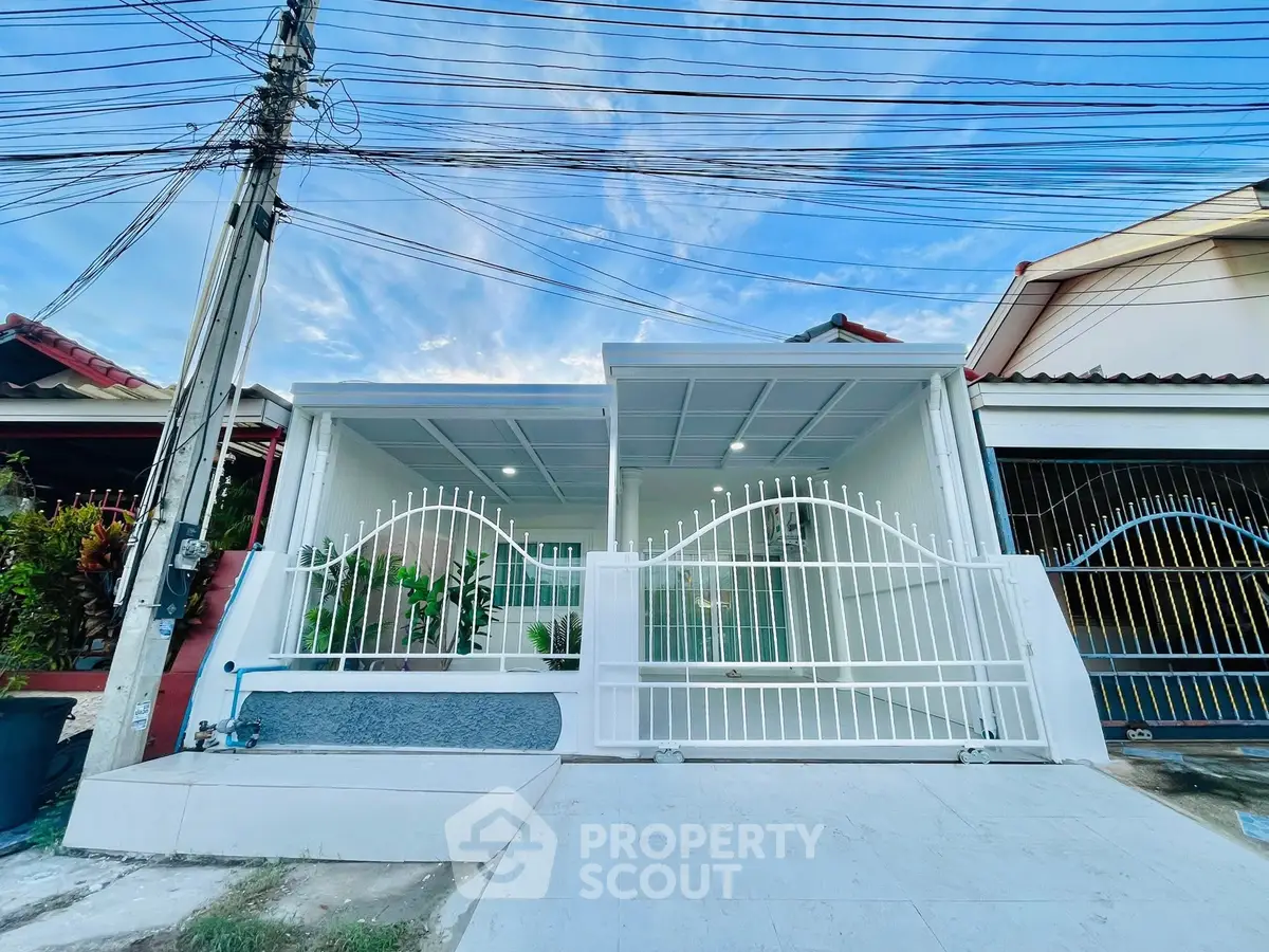 Charming white house with gated entrance and lush greenery, perfect for modern living.