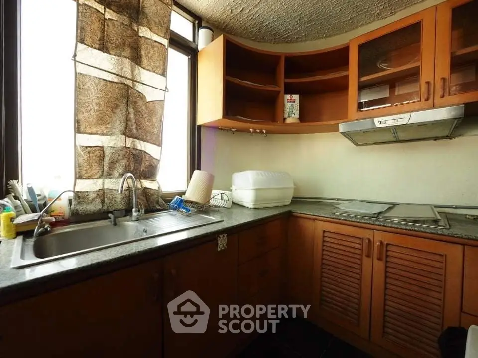 Cozy kitchen with wooden cabinets and large window, perfect for culinary enthusiasts.