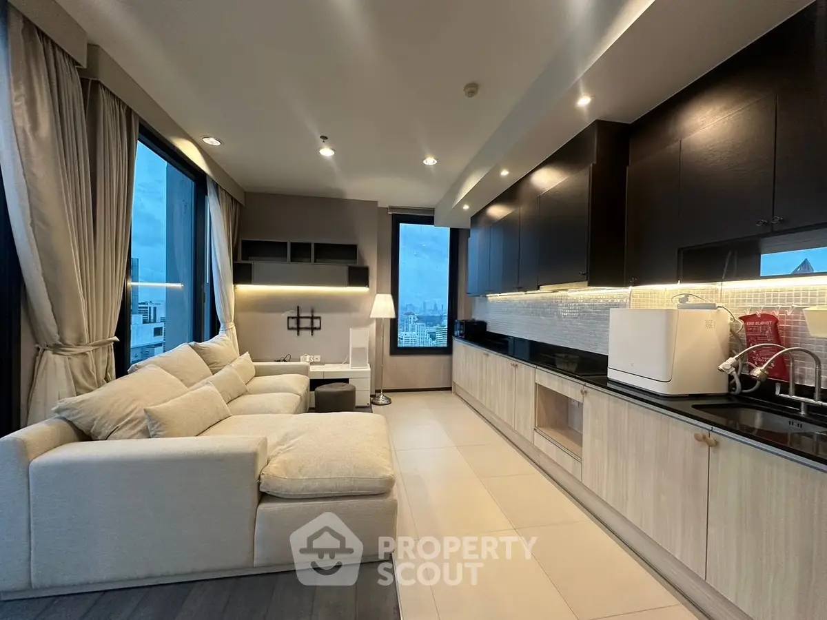 Modern open-layout living room with sleek kitchen and city view, featuring cozy sofa and elegant lighting.