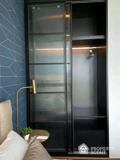 Chic modern bedroom with a sleek black wardrobe featuring stylish ribbed glass doors, complemented by geometric blue wall tiles and elegant gold accents.