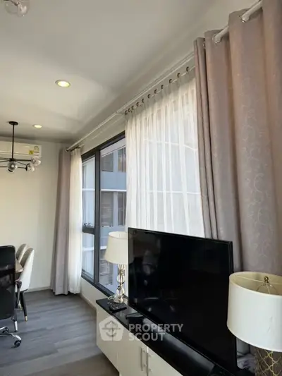 Modern living room with large windows and elegant decor, featuring a TV and stylish lighting.