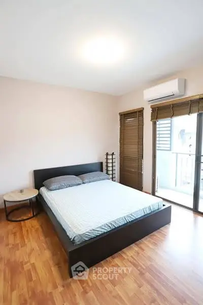 Spacious bedroom with modern decor and balcony access, featuring wooden flooring and ample natural light.