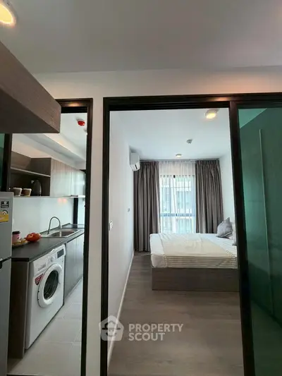 Modern apartment interior with kitchen and bedroom, featuring washing machine and large window.