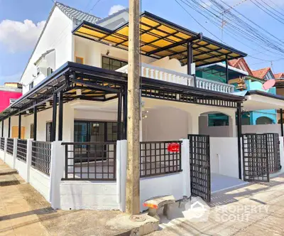 Modern two-story house with spacious balcony and gated entrance in sunny neighborhood.