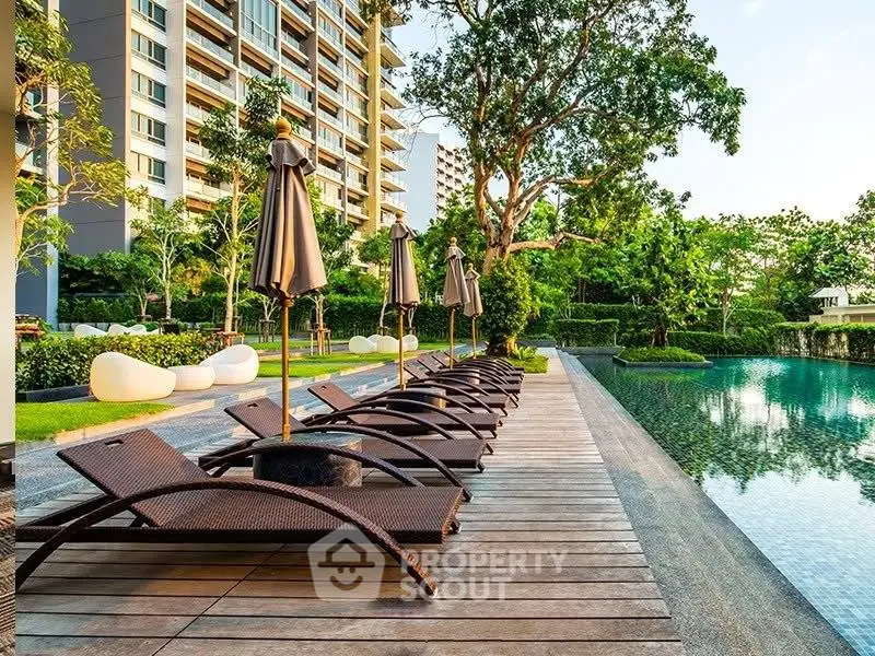 Luxurious poolside area with sun loungers and lush greenery in modern residential complex.