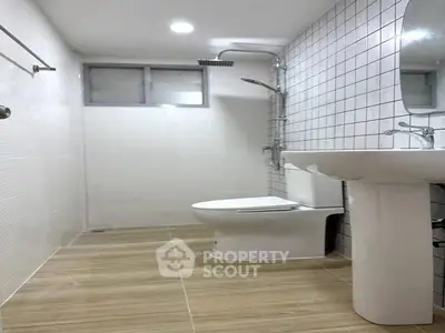 Modern bathroom with sleek fixtures and tiled walls, featuring a shower and pedestal sink.