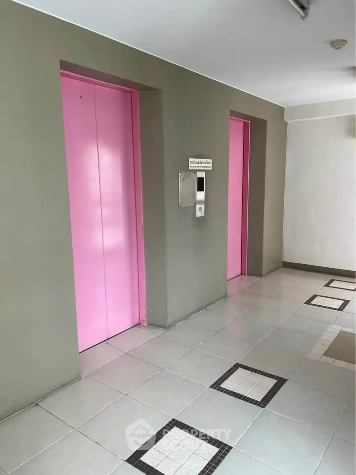Modern building hallway with vibrant pink elevator doors and sleek tile flooring.