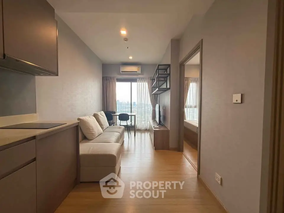Modern apartment interior with open living room and kitchen, featuring a cozy sofa and large window view.