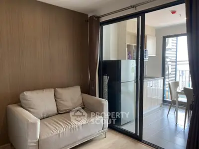 Modern living room with cozy sofa and sliding glass doors leading to a sleek kitchen area.