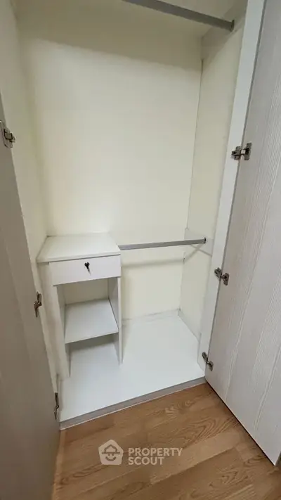 Spacious white closet with wooden flooring, featuring a small built-in drawer and shelf.