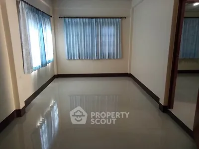 Spacious and well-lit empty room with glossy tiled flooring, large windows with sheer curtains, and a neutral color scheme awaiting personalization.