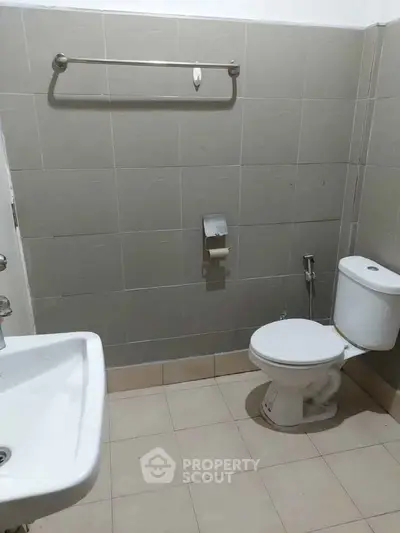 Simple bathroom with tiled walls, toilet, sink, and towel rack, ideal for minimalist design enthusiasts.