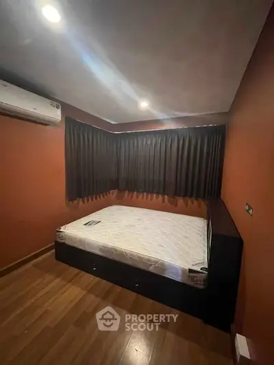 Cozy bedroom with warm lighting and wooden flooring, featuring a comfortable bed and air conditioning.