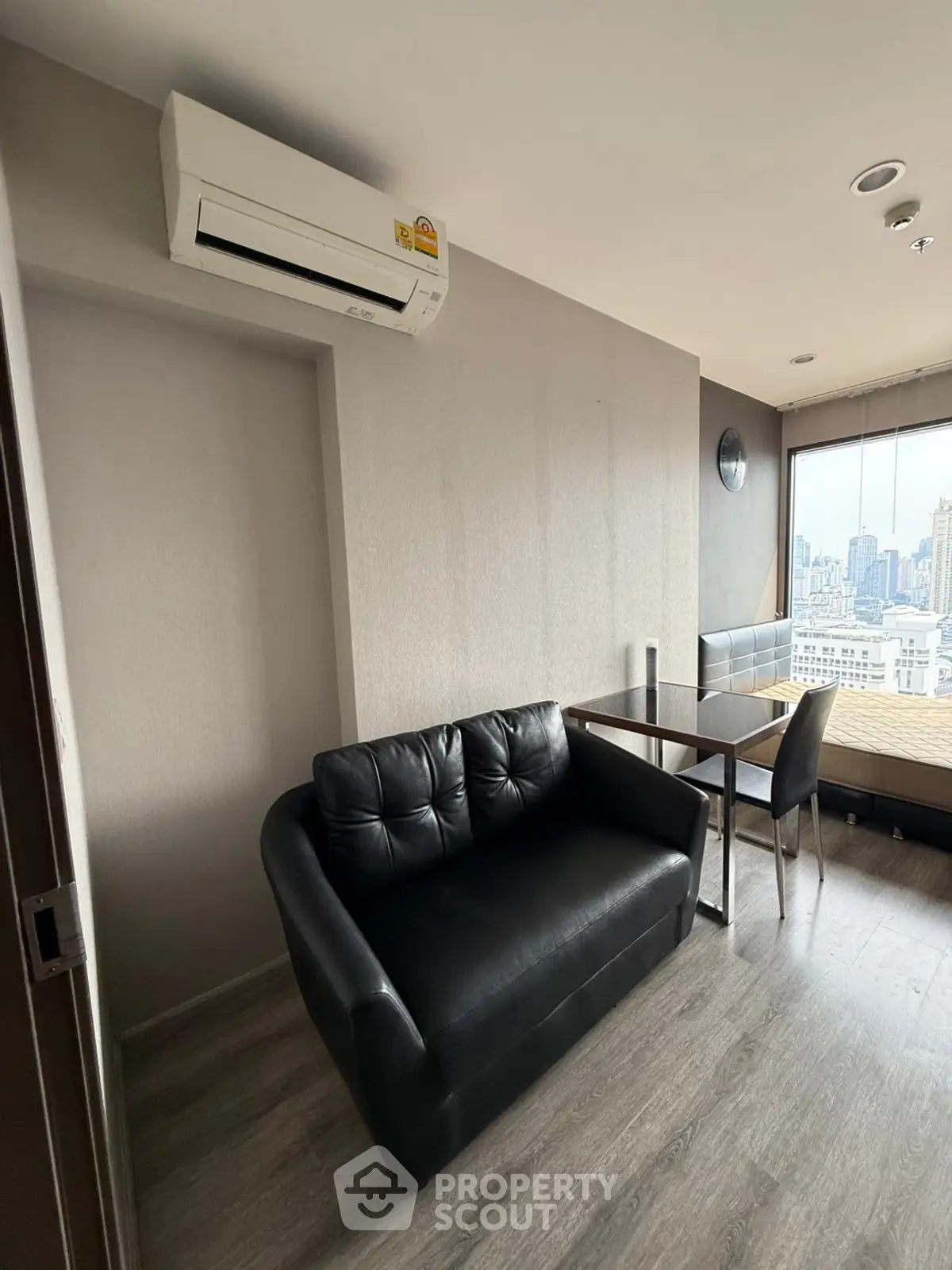 Modern apartment interior with city view, featuring sleek black sofa and dining area.