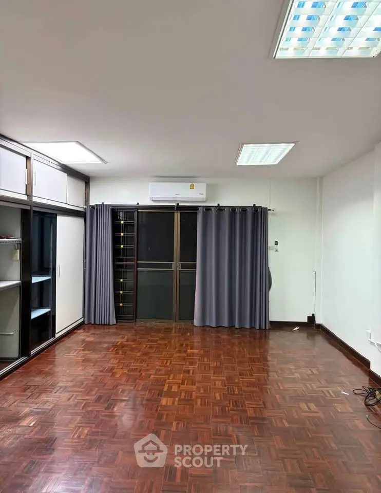 Spacious empty room with wooden flooring and large windows, ideal for customization.