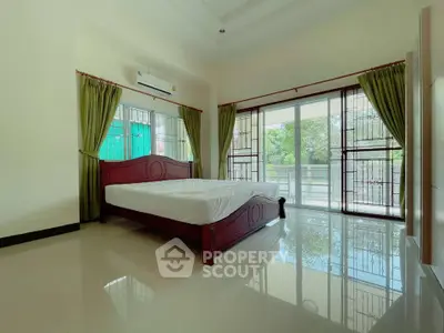 Spacious bedroom with large windows and green curtains, offering a serene garden view.