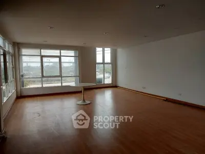 Spacious empty living room with large windows and wooden flooring, offering ample natural light.