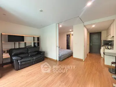 Spacious modern apartment with open living area and cozy bedroom, featuring sleek wooden flooring and contemporary furnishings.