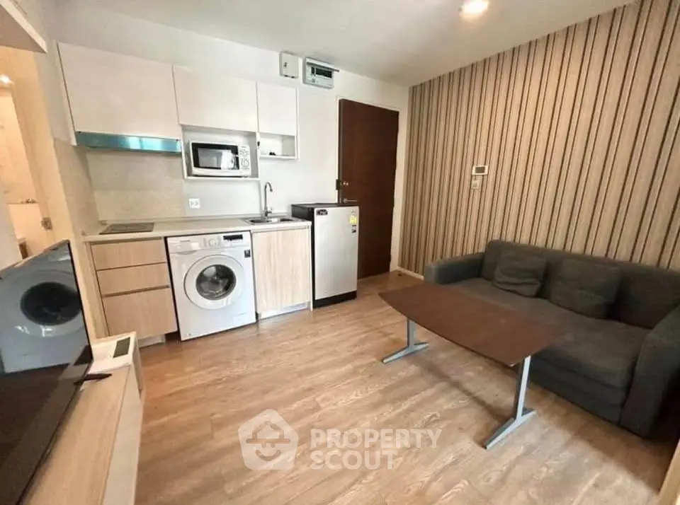 Modern compact living room with integrated kitchen and washing machine, featuring stylish wood flooring.