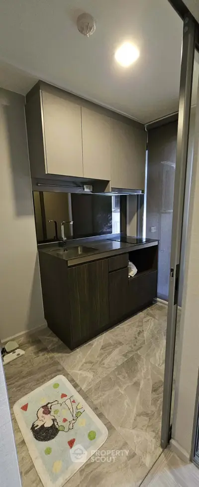 Modern compact kitchen with sleek cabinetry and marble flooring in a stylish apartment.