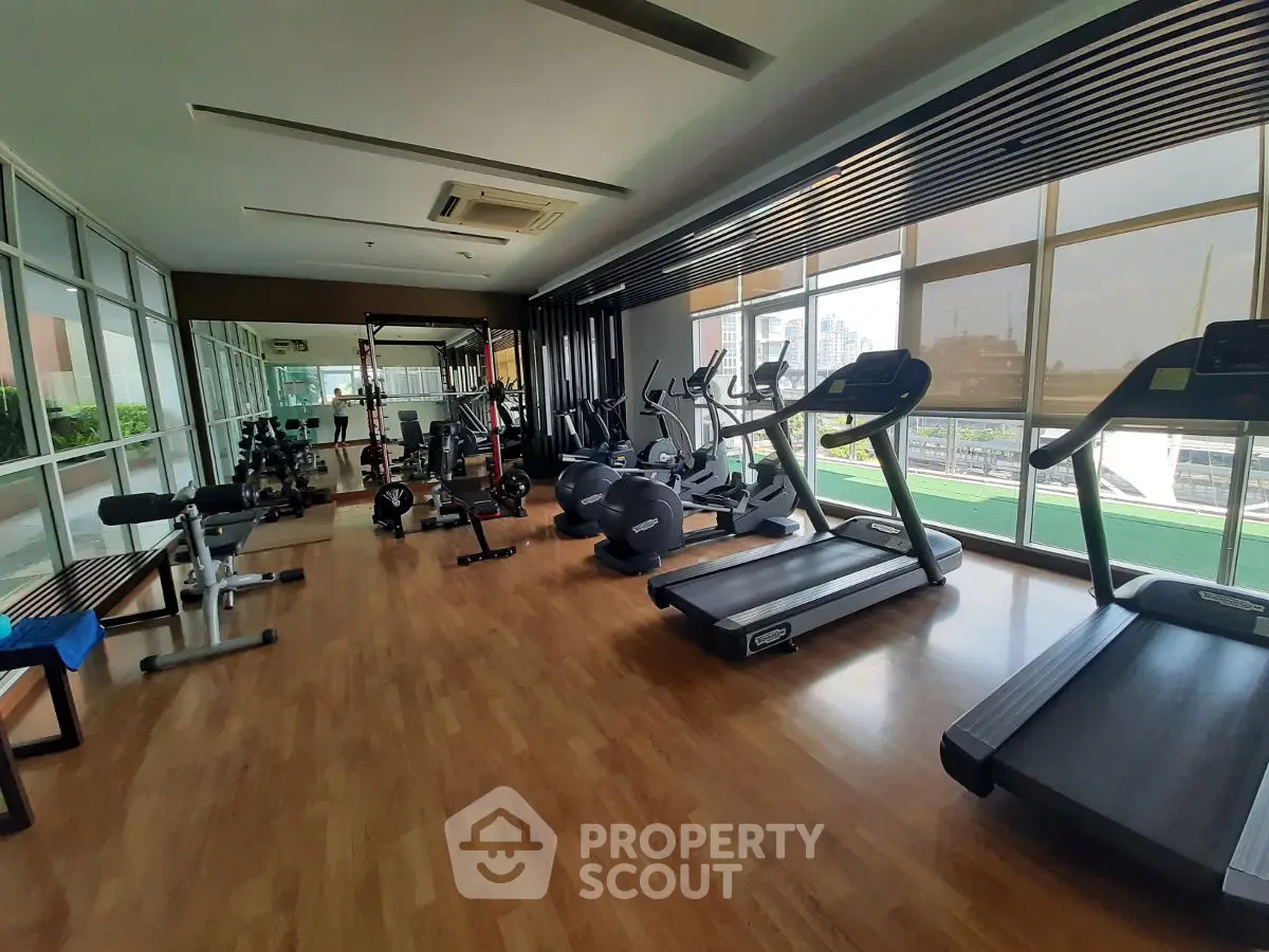 Spacious gym with modern equipment and city view in luxury apartment complex.