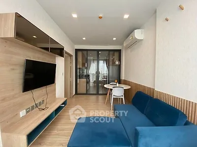 Modern living room with blue sofa and wall-mounted TV, open layout to kitchen area.