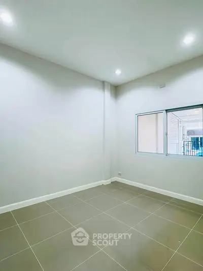Spacious empty room with tiled floor and window, perfect for customization.