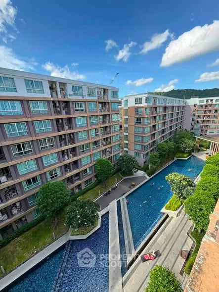 Stunning aerial view of modern apartment complex with large swimming pool and lush greenery.