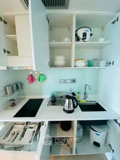 Modern kitchen with sleek white cabinets and built-in appliances, featuring an electric stove and kettle.
