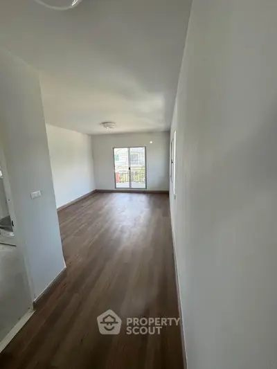 Spacious empty room with wooden flooring and large window for natural light.