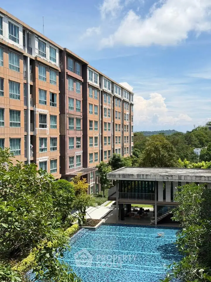 Modern apartment building with lush greenery and inviting swimming pool under a clear blue sky.
