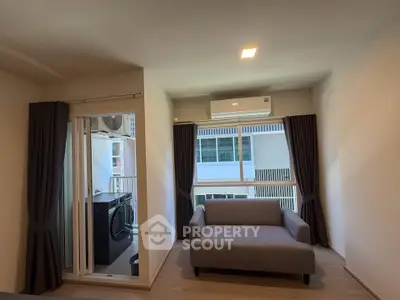 Modern living room with balcony and washing machine, featuring sleek sofa and air conditioning.