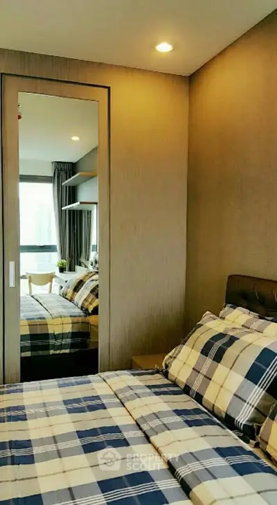 Cozy modern bedroom with stylish plaid bedding and mirrored wardrobe in a contemporary apartment.