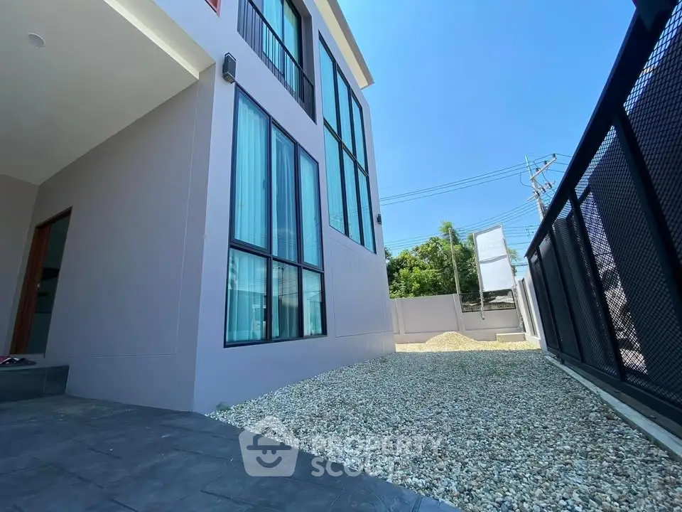 Modern building exterior with large windows and gravel pathway under clear blue sky.