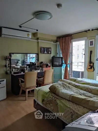 Cozy bedroom with desk, TV, and guitar, featuring natural light and warm decor.
