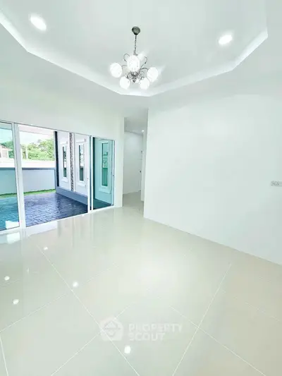 Spacious living room with elegant chandelier and large windows opening to a patio.