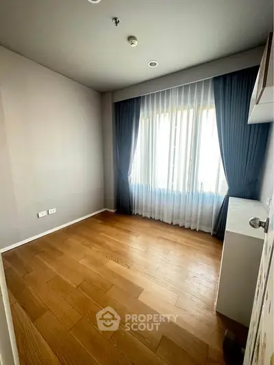 Spacious empty room with wooden flooring and large window, ideal for customization.