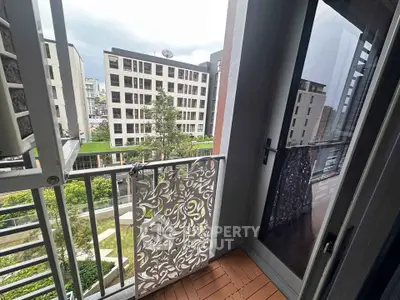 Charming balcony with intricate railing overlooking modern apartment complex and lush greenery.