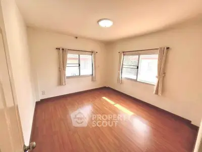 Spacious empty bedroom with wooden flooring and natural light from two windows.
