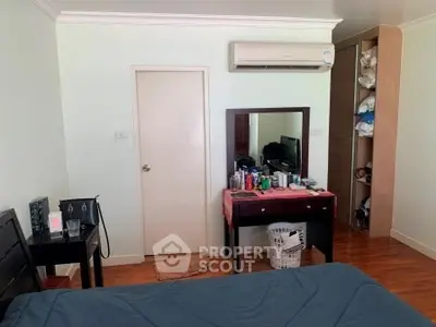 Cozy bedroom with air conditioning and wooden flooring, featuring a vanity and ample storage space.